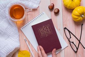 sainte bible dans la main féminine et automne confortable vue de dessus sur fond en bois. concept d'automne d'étude biblique photo
