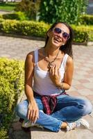 portrait en plein air glamour jeune femme brune avec des lunettes assis sur un banc photo