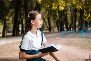 un étudiant à lunettes est distrait de la lecture d'un livre et regarde ailleurs par une chaude journée dans le parc photo