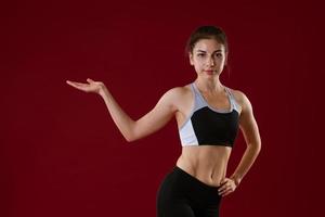 jeune femme en vêtements de sport sur fond rouge montre avec sa main sur le côté photo