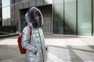 heureuse jeune femme en veste d'hiver avec sac à dos près du bâtiment photo