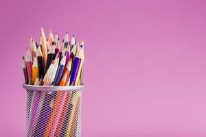 crayons de couleurs différentes dans un verre sur fond rose. photo