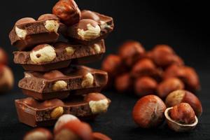 chocolat aux noisettes en forme de tour sur fond sombre, entouré de noix en coque et décortiquées. photo