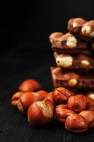 chocolat aux noisettes en forme de tour sur fond sombre, entouré de noix en coque et décortiquées. photo