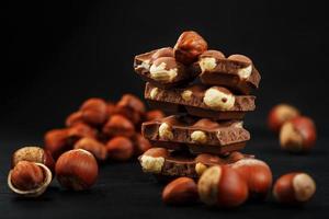 chocolat aux noisettes en forme de tour sur fond sombre, entouré de noix en coque et décortiquées. photo
