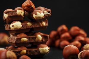 chocolat aux noisettes en forme de tour sur fond sombre, entouré de noix en coque et décortiquées. photo