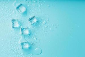 cubes de glace avec des gouttes d'eau éparpillées sur un fond bleu, vue de dessus. photo