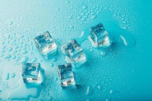 cubes de glace avec des gouttes d'eau éparpillées sur un fond bleu, vue de dessus. photo