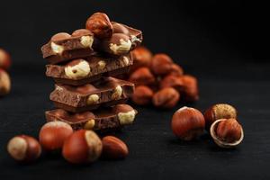 chocolat aux noisettes en forme de tour sur fond sombre, entouré de noix en coque et décortiquées. photo