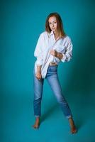 jeune femme posant en chemise blanche et jeans sur fond bleu photo