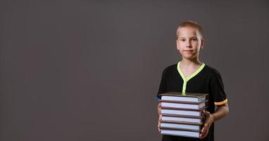 garçon d'écolier tenant une pile de livres sur un fond gris photo