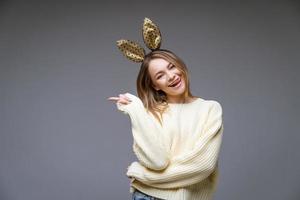 jeune femme dans des oreilles de lapin montre la langue et le doigt sur le côté en arrière-plan photo