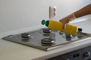 une main humaine dans un gant en caoutchouc blanc lave la cuisinière à gaz avec un détergent. photo