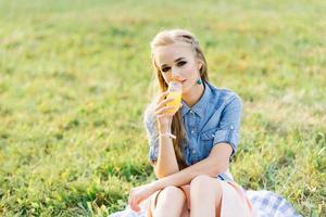 portrait d'une jeune femme buvant du jus d'orange dans un verre dans un parc extérieur pique-nique d'été photo