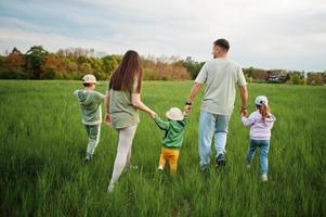 dos de parents marchant avec trois enfants s'amusant ensemble au pré. photo