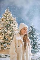 jolie fille blonde caucasienne en manteau de fourrure écologique blanc, chapeau et gants marchant dans la forêt de noël d'hiver. nouvel an, conte de fées, concept de mode photo