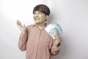 une jeune femme heureuse porte une chemise rose et tient de l'argent liquide en roupie indonésienne isolée par fond blanc photo