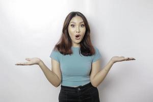 femme asiatique choquée portant un t-shirt bleu pointant vers l'espace de copie à côté d'elle, isolée par fond blanc photo