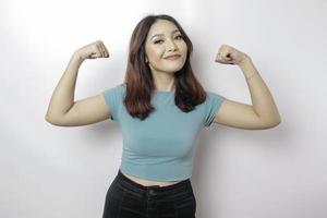 femme asiatique excitée portant un t-shirt bleu montrant un geste fort en levant les bras et les muscles en souriant fièrement photo