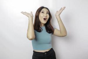 femme asiatique choquée portant un t-shirt bleu pointant vers l'espace de copie au-dessus d'elle, isolée par fond blanc photo