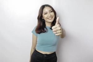 femme asiatique excitée portant une chemise bleue donne le pouce vers le haut geste de la main d'approbation, isolée par fond blanc photo