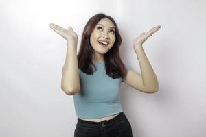 femme asiatique excitée portant un t-shirt bleu pointant vers l'espace de copie au-dessus d'elle, isolée par fond blanc photo