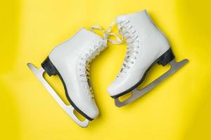 concept vacances d'hiver. patins artistiques blancs sur fond jaune. photo