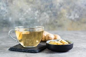 thé au gingembre dans une tasse et racine hachée dans un bol sur la table. vitamines naturelles. photo