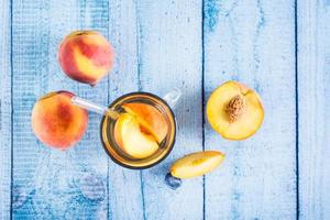 compote de pêches dans un verre avec une paille et des fruits sur la table. boissons bio d'été. vue de dessus photo