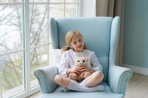 jolie fille caucasienne est assise dans un fauteuil bleu près de la fenêtre à la maison dans la chambre photo