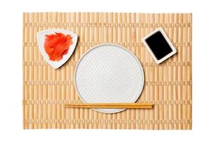 assiette blanche ronde vide avec des baguettes pour sushi et sauce soja, gingembre sur fond de natte de bambou jaune. vue de dessus avec espace de copie pour votre conception photo