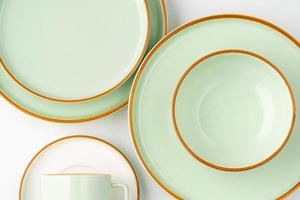 un ensemble de vaisselle en céramique blanche et vert pastel aux contours orange. vue de dessus photo