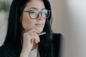 une femme auteur sérieuse travaille sur une nouvelle publication, concentrée sur l'affichage de l'ordinateur, garde le stylo à la main, porte des lunettes pour la correction des yeux. une femme entrepreneur ambitieuse et prospère gère une entreprise photo