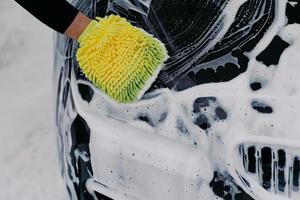 un homme méconnaissable lave une voiture noire savonneuse avec un chiffon à la gare. un ouvrier nettoie l'automobile. concept de véhicule et de service photo