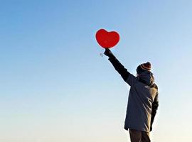 jeune homme de dos avec un ballon en forme de coeur rouge contre le ciel bleu. concept de la saint-valentin, espace de copie photo