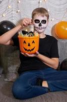 un garçon en maquillage squelette sort des bonbons d'une fête d'halloween. photo