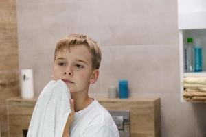 reflet d'un écolier essuyant son visage avec une serviette après s'être lavé dans la salle de bain. photo