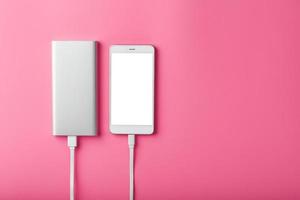 powerbank charge un smartphone sur fond rose. batterie externe universelle pour espace libre de gadgets et composition minimaliste. photo