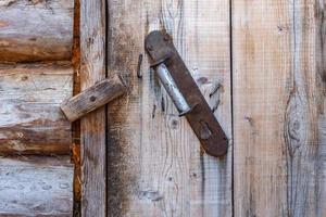 poignée en fer sur un mur en bois. la porte est fermée par un loquet en bois. photo