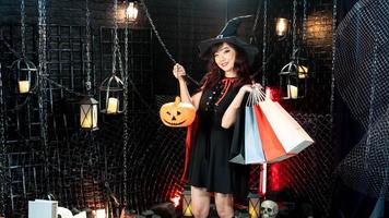 fille d'halloween portant un costume de sorcière avec un chapeau tenant une citrouille lanterne et un sac à provisions sur le thème d'halloween photo