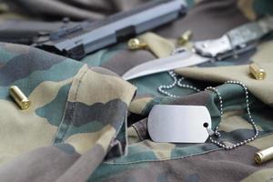 Jeton d'étiquette de chien de l'armée avec des balles de 9 mm et un pistolet allongé sur un tissu vert camouflage plié photo