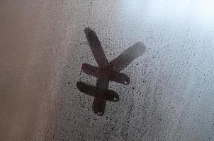 le symbole du yen chinois est écrit avec un doigt sur la surface du verre embué photo