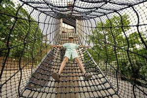 garçon jouant dans des cordes de toboggan de fusée à l'aire de jeux pour enfants dans un parc public. photo