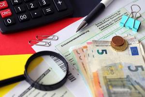 Le formulaire de déclaration de revenus allemand avec un stylo et des billets en euros européens se trouve sur le drapeau de près. contribuables allemands utilisant l'euro pour payer leurs impôts photo
