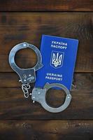 un passeport ukrainien avec des menottes de police se trouve sur une table en bois. problèmes avec la loi lors du franchissement des frontières des pays. le côté illégal du voyage sans visa pour les citoyens ukrainiens photo