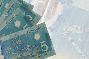 5 billets de dollars canadiens sont empilés sur fond de gros billets semi-transparents. arrière-plan abstrait des affaires photo