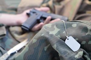le jeton de l'armée repose sur l'uniforme de camouflage du soldat mort et la main avec un pistolet photo