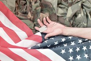 Perles militaires argentées avec étiquette de chien et main de soldat mort sur le drapeau en tissu des États-Unis et uniforme de camouflage photo