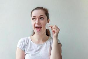 femme souriante avec une peau douce et saine enlevant le maquillage avec un tampon de coton isolé sur fond blanc photo