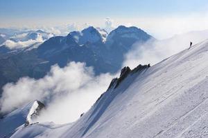 Grimpeur sur une crête de montagne couverte de neige avec des nuages tourbillonnants